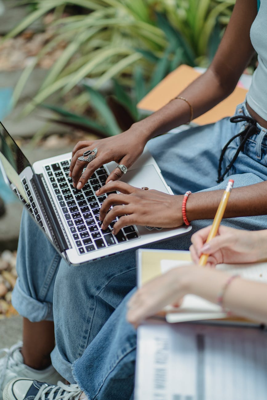 female friends using netbook with notepad on bench